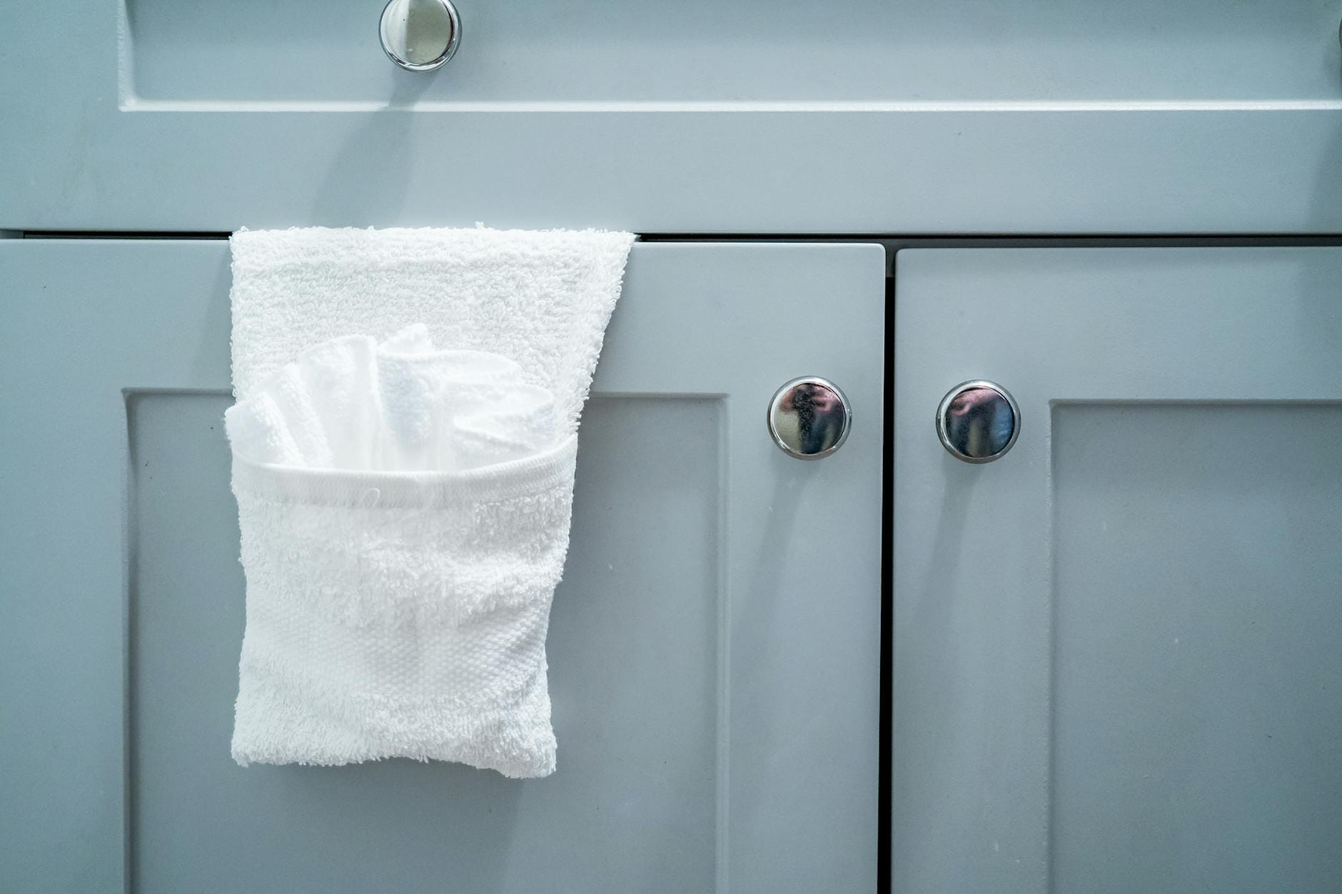 Biały ręcznik zawieszony na drzwiach nowoczesnej szarej szafki łazienkowej