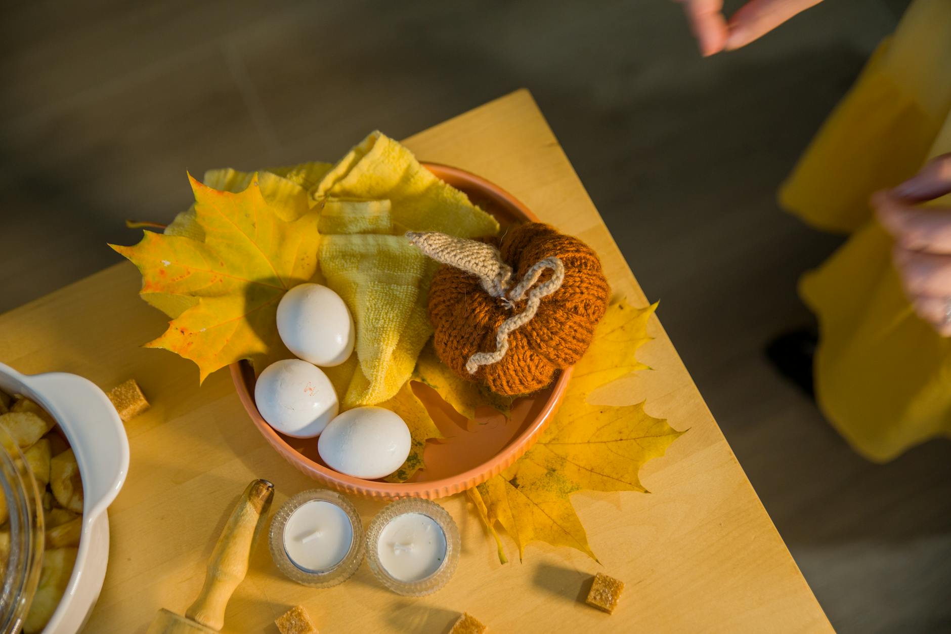 Dzianinowa dynia, jajka i świece na rustykalnym stole w jesiennych liściach
