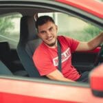 Uśmiechnięty młody kierowca prowadzi czerwone auto z zapiętym pasem bezpieczeńst
