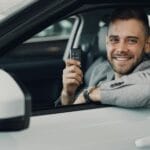 Uśmiechnięty młody kierowca w aucie trzyma kluczyki do samochodu