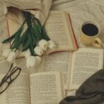 Książki, białe tulipany, kubek kawy i okulary na łóżku